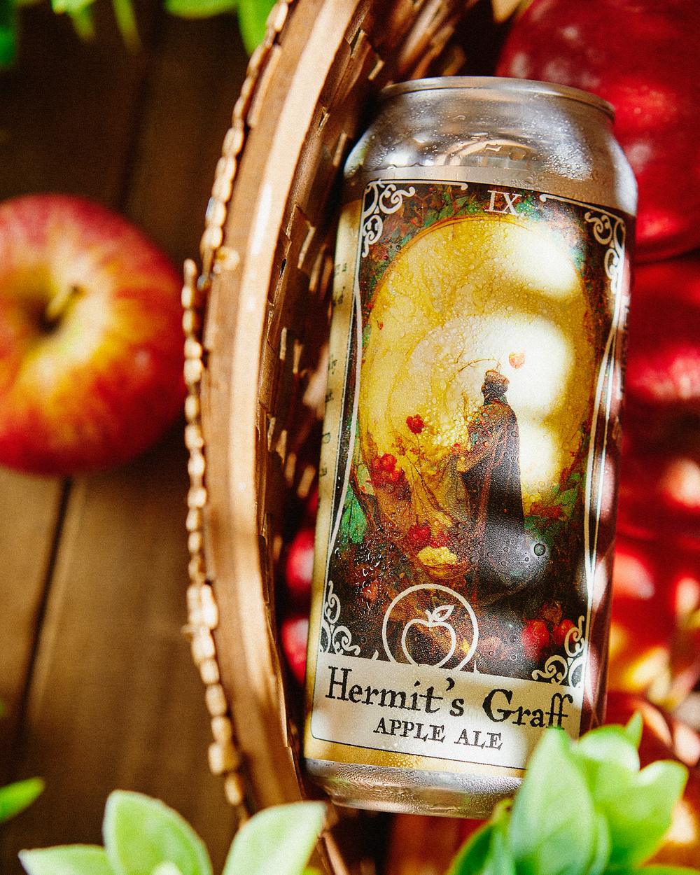 Hermit's Graff apple ale can, its label illustrated as a tarot card, in a basket of apples